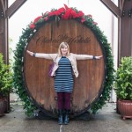 Kim extending arms out to try to touch the sides of a massive wine barrel